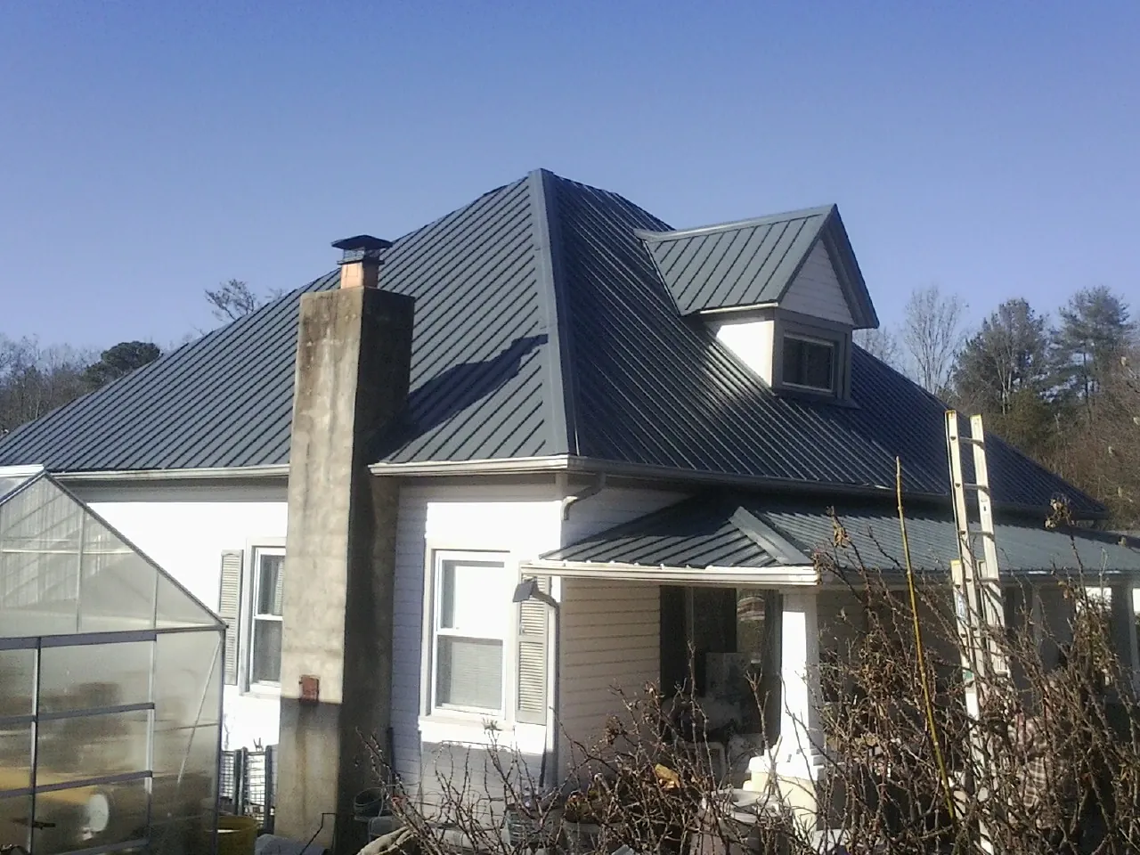 Dark blue standing seam metal roof on a white farmhouse with dormer — Slate & Tile Roof Repair by Roofing Brothers in Olivia