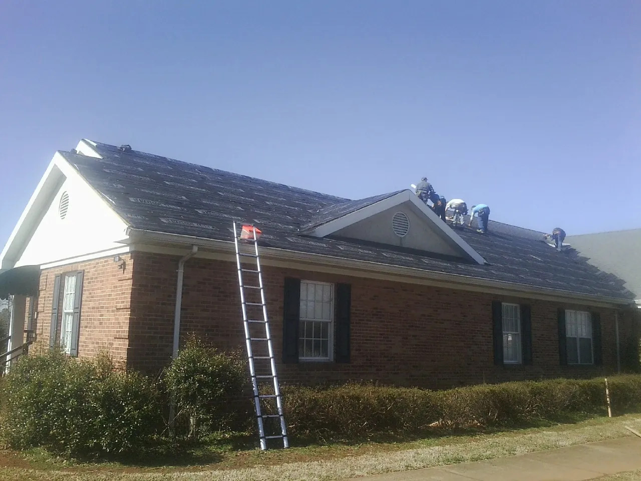 Crew tearing shingles off a brick ranch roof with a ladder set — Emergency Roof Repair work by our crew in Olivia