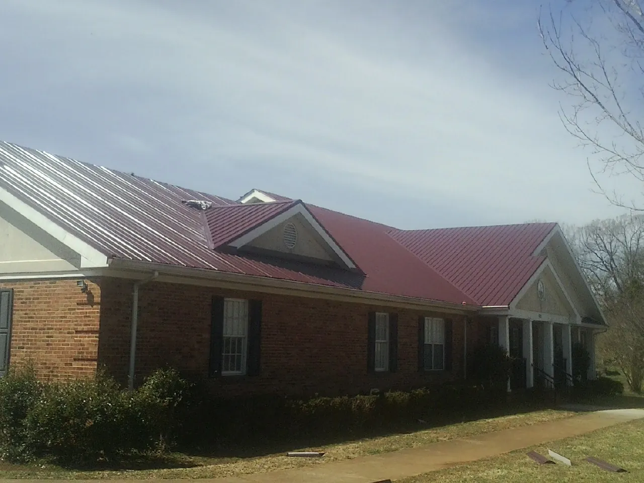 Red metal roof with gabled entries on a long brick building, from a Hail Damage Roof Repair job in Olivia