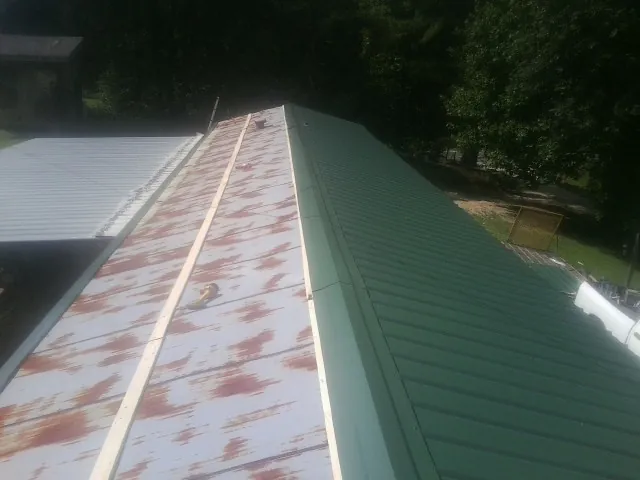 Old rusted panels beside newly installed green metal roofing — Wind Damage Roof Repair by Roofing Brothers in Olivia