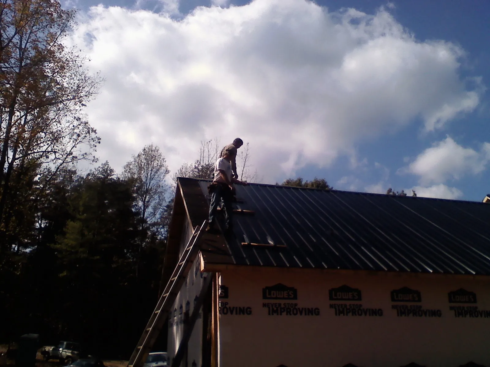 Roofer fastening dark metal panels high against a cloudy sky, from a Roof Inspection job in Olivia